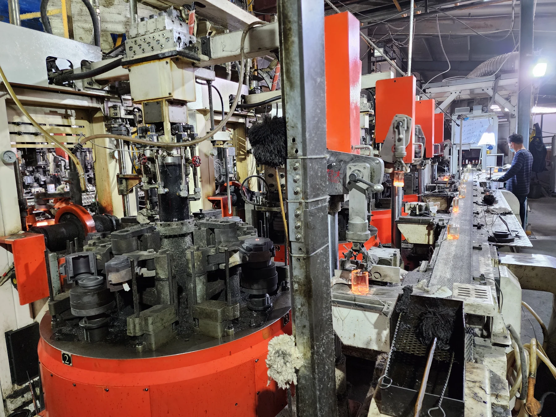 Hot glass vessels moving past forming equipment in a workshop